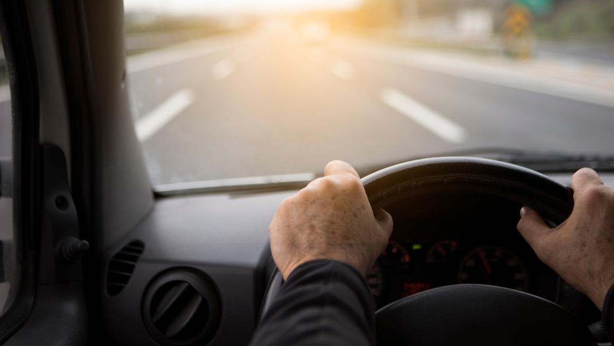 Dłonie na kierownicy mężczyzny jadącego przepisowo, tak by nie otrzymać punktów karnych.